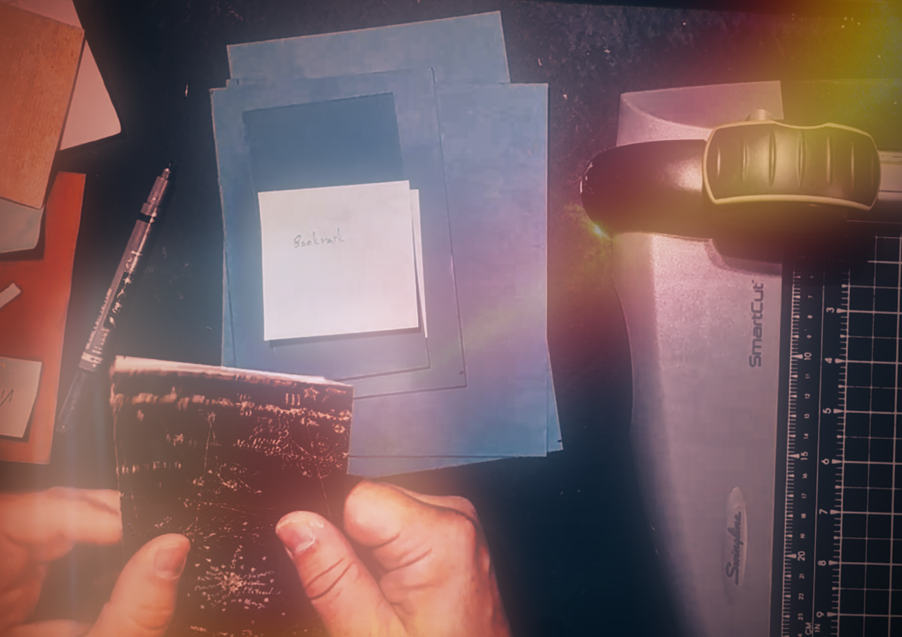 a notebook covered with astronomic notations is held in hands with other papers, cutters, and pens in the background.