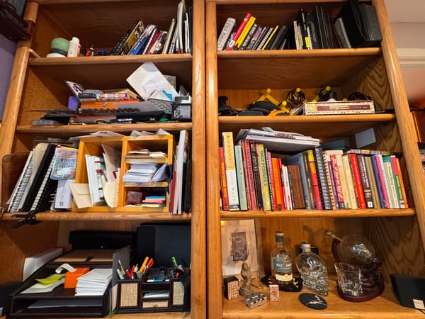 A bookshelf packed with papers, books, cables, very disorganized.